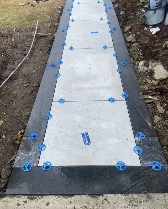 Porcelain path with a dark border being laid with blue tile levelling clips