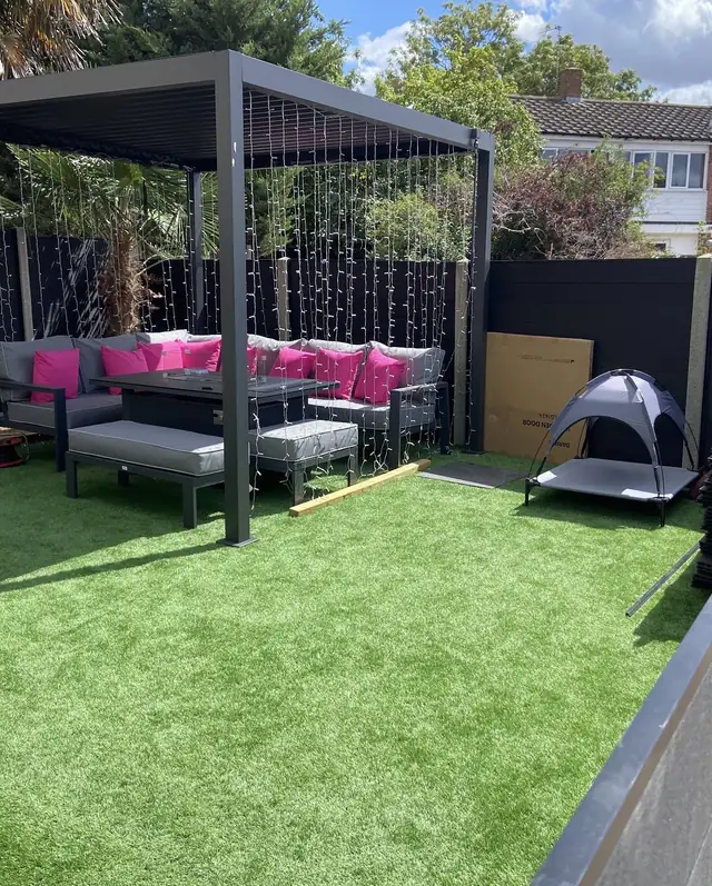 Artificial lawn laid around a covered pergola seating area with dark fencing