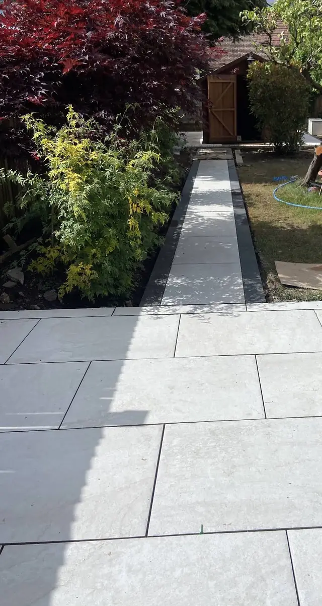 New pale porcelain patio with a bordered path leading down the garden to a shed