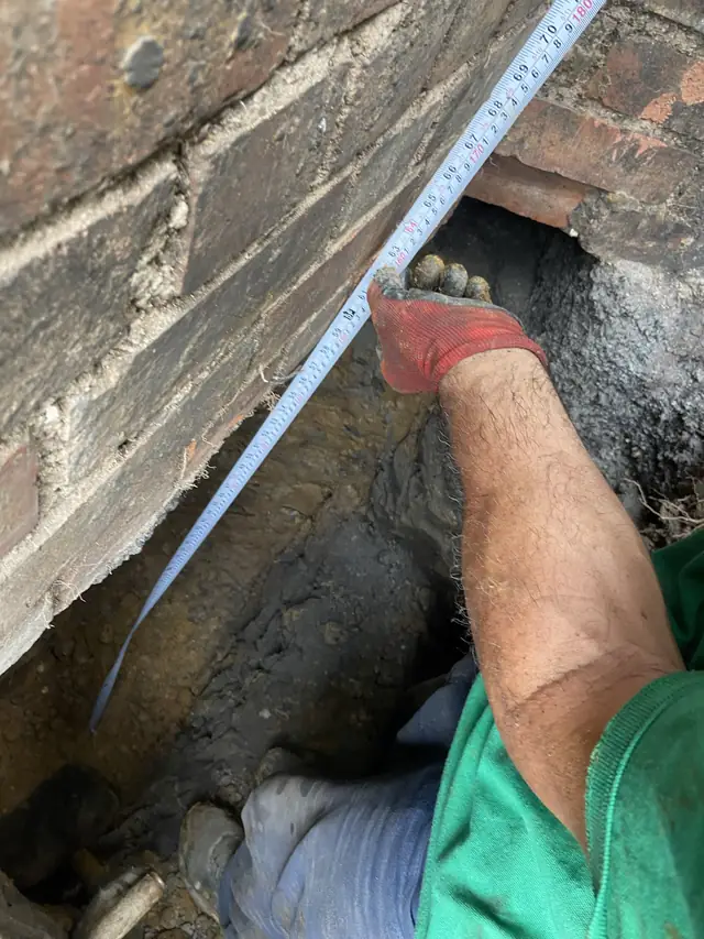Checking the depth of an excavation under a brick wall with a tape measure